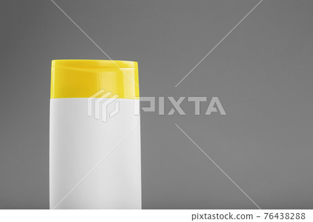 White plastic bottle with yellow cap with shampoo gel on gray background 76438288