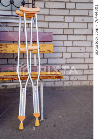 Underarm crutches against the background of a brick wall near the bench. Underarm crutches against the background of a brick wall near the bench. 76444001