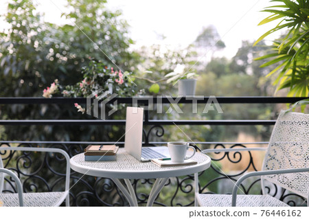 Coffee cup with laptop and notebook on white metal table decorated with plant pot outdoor balcony view Coffee cup with laptop and notebook on white metal table decorated with plant pot outdoor balcony view 76446162