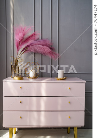 light pink dresser at the gray wall decorated with candles and colored feathers. 76447174