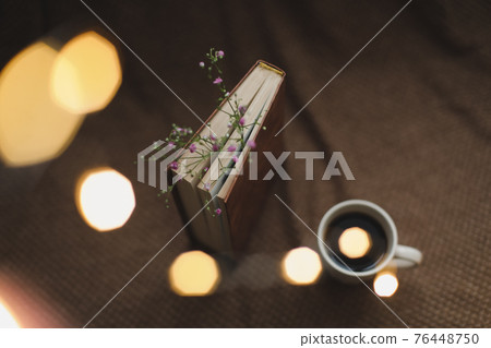 A book with flowers and cup of coffee on dark background top view 76448750