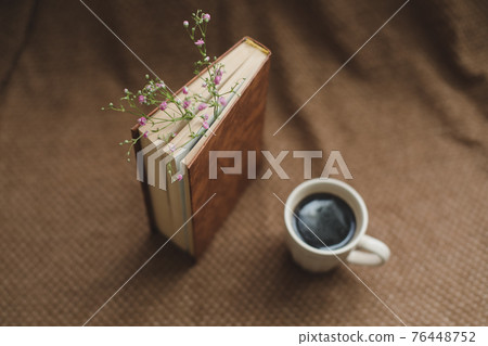 A book with flowers and cup of coffee on dark background top view 76448752