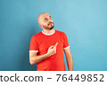A middle-aged man with a beard in a red T-shirt on a blue background stands rejoicing in victory. Isolated. 76449852