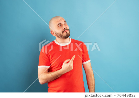 A middle-aged man with a beard in a red T-shirt on a blue background stands rejoicing in victory. Isolated. A middle-aged man with a beard in a red T-shirt on a blue background stands rejoicing in victory. Isolated. 76449852
