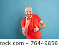 A middle-aged man with a beard in a blue T-shirt on a red background stands rejoicing in victory. Isolated. 76449856