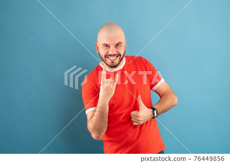 A middle-aged man with a beard in a blue T-shirt on a red background stands rejoicing in victory. Isolated. 76449856