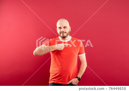 A middle-aged man with a beard in a red T-shirt on a red background stands rejoicing in victory. Isolated. A middle-aged man with a beard in a red T-shirt on a red background stands rejoicing in victory. Isolated. 76449858