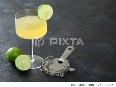 Gimlet Kamikaze cocktail in modern glass with lime slice black board with fresh limes and strainer. Gimlet Kamikaze cocktail in modern glass with lime slice black board with fresh limes and strainer. 76449996
