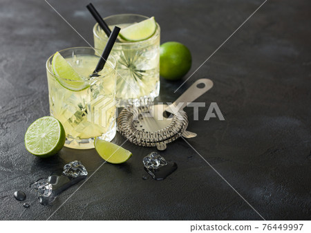 Gimlet Kamikaze cocktail in crystal glasses with lime slice and ice on black board with fresh limes and strainer. Gimlet Kamikaze cocktail in crystal glasses with lime slice and ice on black board with fresh limes and strainer. 76449997