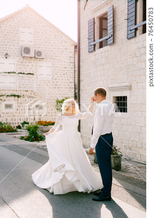 The bride and groom are dancing on the road near the beautiful white house in the old town of Perast The bride and groom are dancing on the road near the beautiful white house in the old town of Perast 76450783