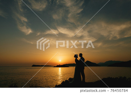 The bride and groom are embracing on the seashore at sunset and look at each other  76450784