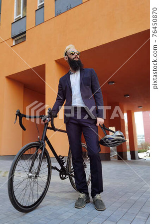 A young stylish businessman pushing a bicycle while going to work. 76450870