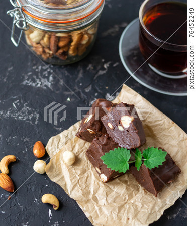 Homemade chocolate fudge garnished with mint leaves and served with tea on a black background. Nuts in the background blurred background. Copy space. Homemade chocolate fudge garnished with mint leaves and served with tea on a black background. Nuts in the background blurred background. Copy space. 76452249