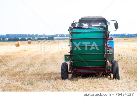 tractor makes big straw roll on yellow field at summer day tractor makes big straw roll on yellow field at summer day 76454127