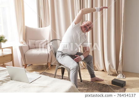Senior caucasian man stretching side sitting on chair at his living room. Senior caucasian man stretching side sitting on chair at his living room. 76454137
