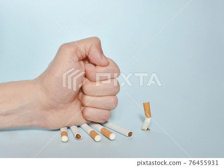 Hand destroying cigarettes on blue background. Quit smoking, World No Tobacco Day on May 31 concept. Selective focus 76455931