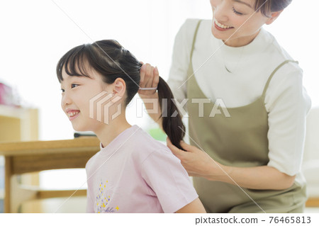 A girl who has her mother tie her hair 76465813