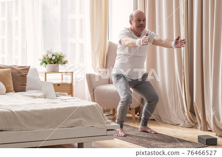Senior man practicing yoga at home doing Chair pose, Utkatasana Senior man practicing yoga at home doing Chair pose, Utkatasana 76466527