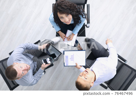 Business partners are sitting at table smiling and looking up Business partners are sitting at table smiling and looking up 76467496