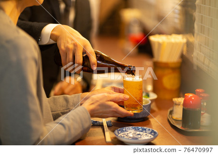 Hands pouring beer into a glass at a tavern Hands pouring beer into a glass at a tavern 76470997