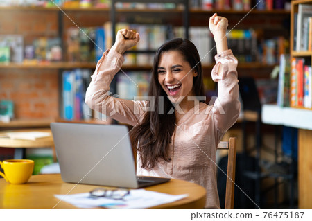 Lucky day. Emotional latin woman celebrating success in front of laptop at cafe, clenching fists and screaming Lucky day. Emotional latin woman celebrating success in front of laptop at cafe, clenching fists and screaming 76475187