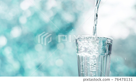Pouring Clean Drinking Water into a Glass. Blurred Nature Tree as background. Surreal Color Tone. Front View. Minimal with Empty for Copy Space Pouring Clean Drinking Water into a Glass. Blurred Nature Tree as background. Surreal Color Tone. Front View. Minimal with Empty for Copy Space 76478131