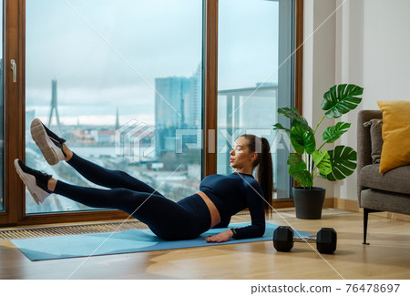 Slender woman practices abdominal exercises on blue mat 76478697