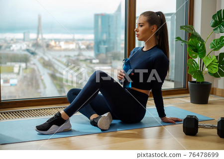 Sportive brunette with water bottle in hand sits on mat 76478699
