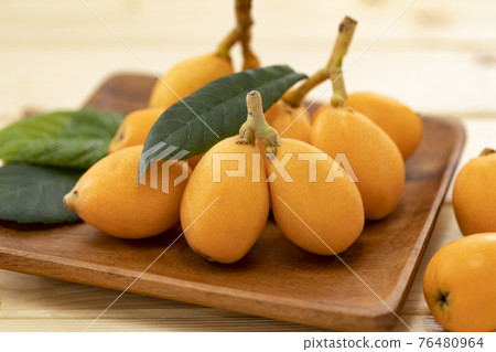 Loquat _ background blur arranged with leaves on a wood grain table Loquat _ background blur arranged with leaves on a wood grain table 76480964