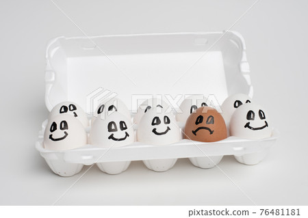 tray full of smile white eggs and only one different sad orange egg. tray full of smile white eggs and only one different sad orange egg. 76481181