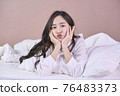 Cute young woman lying on bed playing with blanket and looking at camera. Happy Asian girl feeling fresh after nap on bed. Laughing woman having fun while embracing pillow and blanket. 76483373