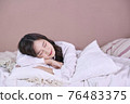 Beautiful young Asian woman lying down in the bed and sleeping. Teen girl with closed eyes covers her face with white blanket in the morning 76483375