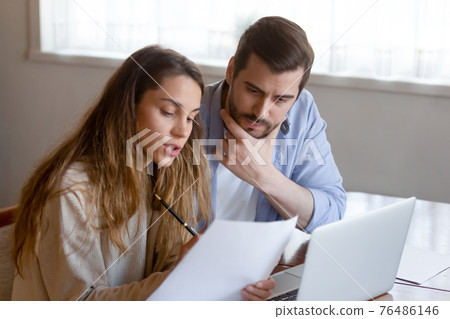 Pensive couple pay online on laptop considering paperwork 76486146