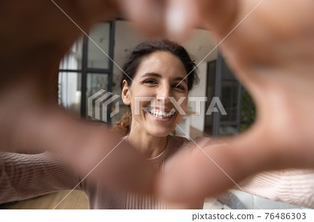 Hispanic female looking at camera through heart of joined fingers. Hispanic female looking at camera through heart of joined fingers. 76486303