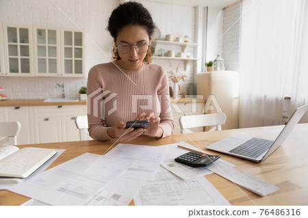 Young hispanic female use modern phone laptop for home accounting Young hispanic female use modern phone laptop for home accounting 76486316