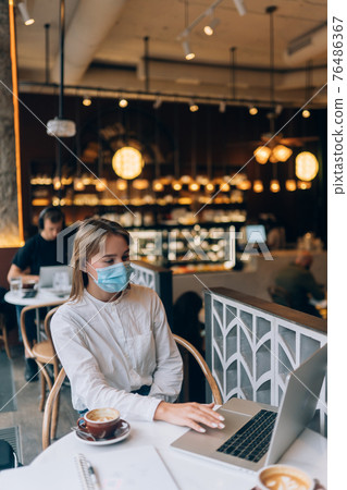 Pretty woman wearing medical face mask, using laptop to work. Pretty woman wearing medical face mask, using laptop to work. 76486367