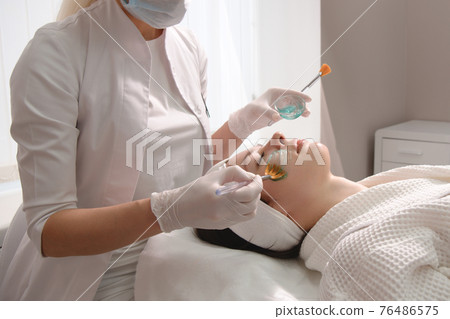 Facial skincare. A mask is applied to a woman's face in a cosmetology clinic. Close up 76486575