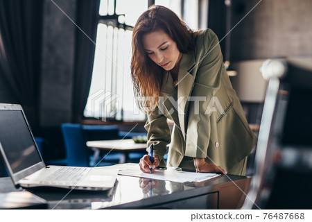 Woman entrepreneur stands and writes leaning on desk 76487668