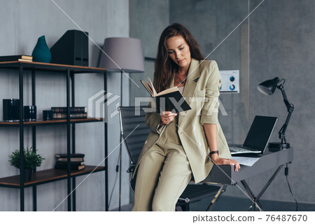 Businesswoman in the office stands at her desk and reads her notebook. 76487670