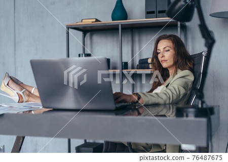 Woman works sitting with her legs up on her desk Woman works sitting with her legs up on her desk 76487675