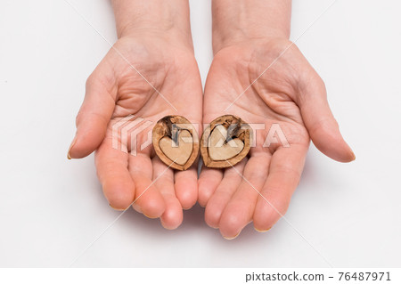 The woman's hands hold two halves of walnut in the form of a heart on a white background, isolated 76487971