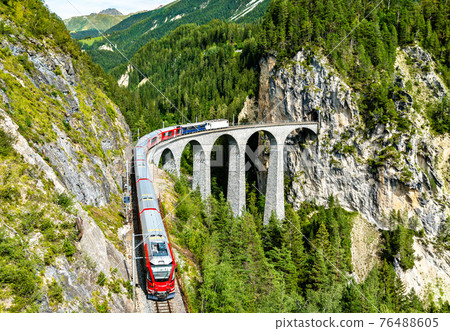 Passenger train crossing the Landwasser Viaduct in Switzerland 76488605
