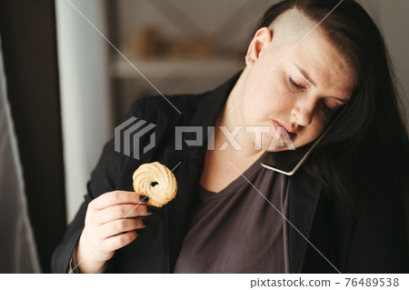 Woman multitasking eating sweets at her workplace 76489538