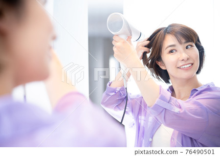A woman who dries her hair while looking in the mirror A woman who dries her hair while looking in the mirror 76490501