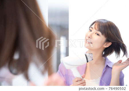 A woman who dries her hair while looking in the mirror 76490502