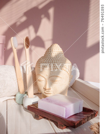 White Buddha bust on pastel pink background decorated with shades. Zero waste bamboo toothbrush. Spa asian style. Relax mood. Yoga background. Eco friendly  76491893