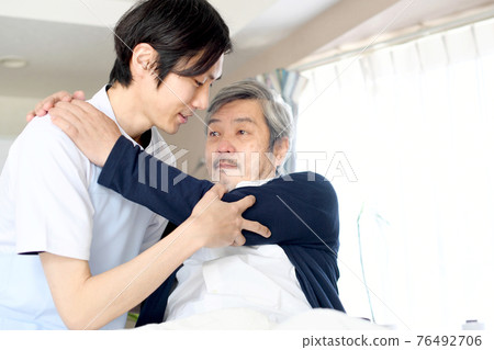 Caregiver man waking up an elderly man in bed Caregiver man waking up an elderly man in bed 76492706