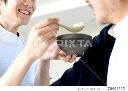 A young man in an apron helping a senior man with a meal 76493525
