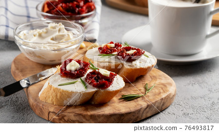 Homemade sandwiches with cream cheese and sun-dried tomatoes on a wooden board of olive - delicious healthy breakfast, italian cuisine 76493817