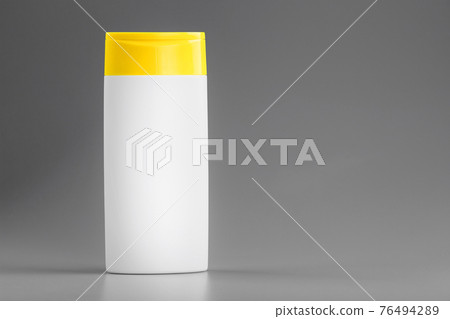 White bottle of shampoo and shower gel with yellow cap on gray background 76494289